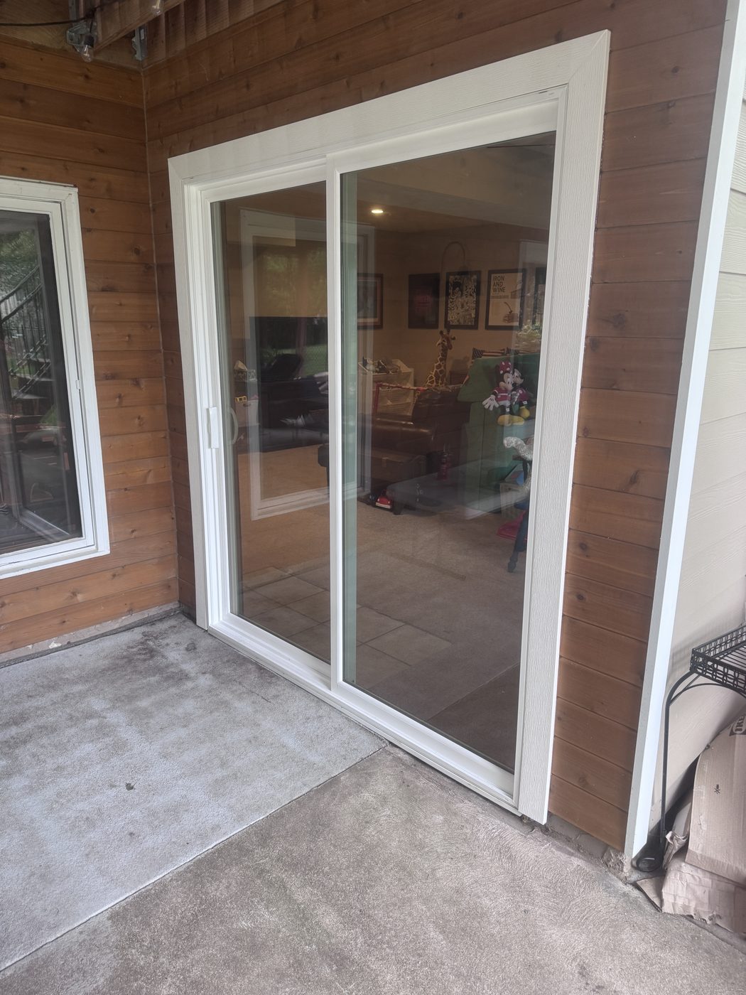 The new sliding patio door from the patio side, set neatly into the cedar siding with fresh white trim
