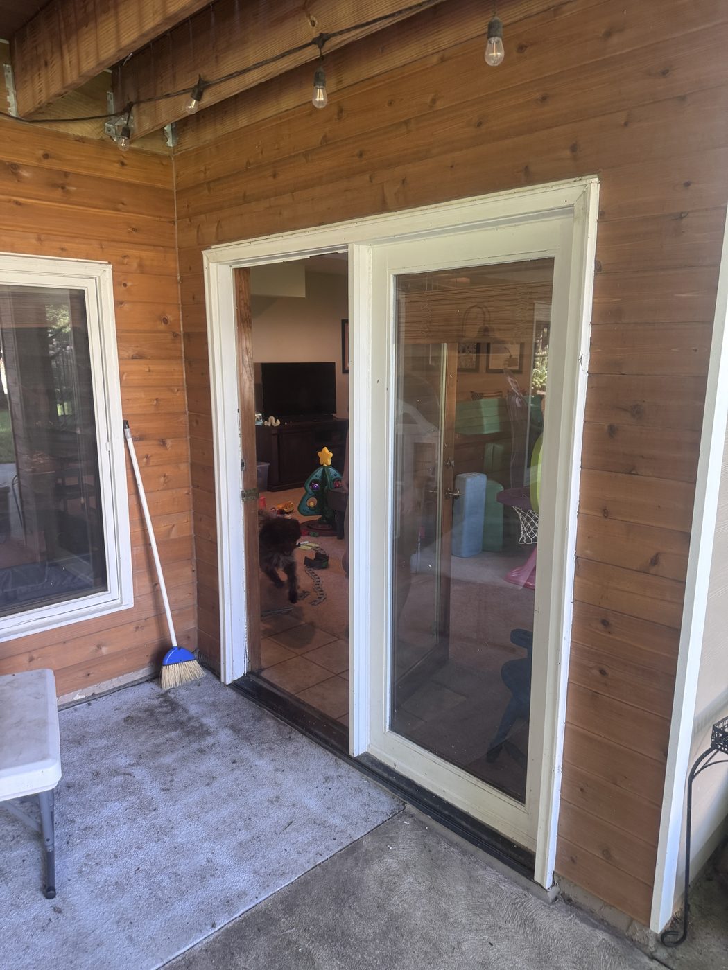 The same old patio door from the patio side — weathered white-painted frame against the cedar siding, showing its age