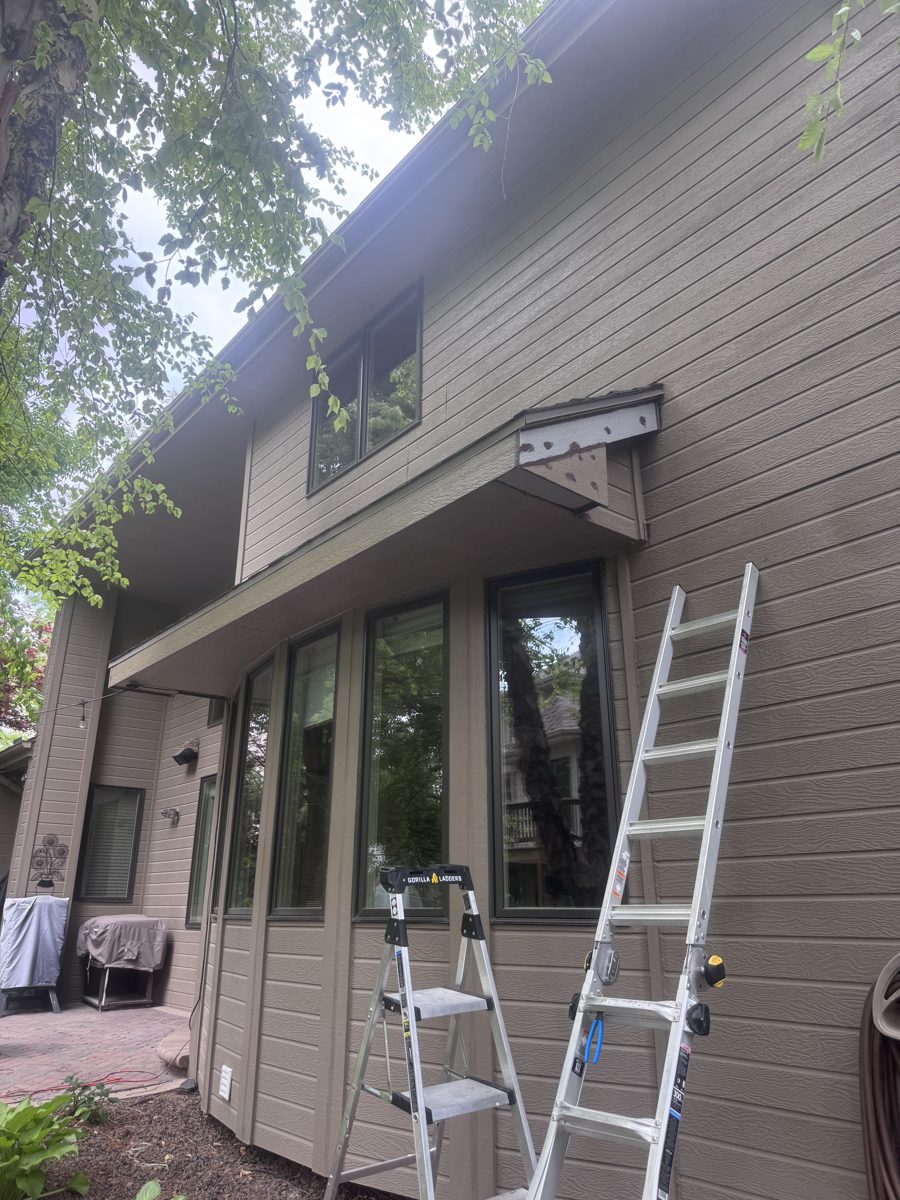 A wider view of the same home with ladders staged, the rotted corner cut back and rebuilt with fresh wood, ready for primer and paint